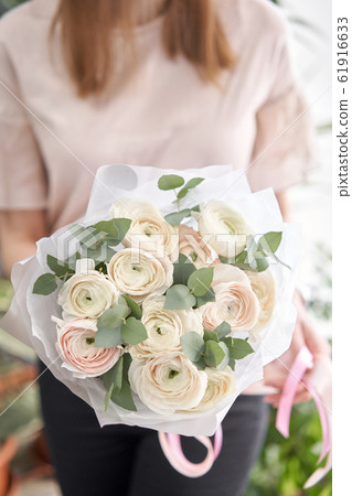 Persian buttercup in womans hands. Bunch pale pink ranunculus flowers with green eucalyptus. The work of the florist at a flower shop Persian buttercup in womans hands. Bunch pale pink ranunculus flowers with green eucalyptus. The work of the florist at a flower shop 61916633
