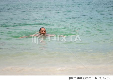 A man swims in the waves of the sea or ocean in a A man swims in the waves of the sea or ocean in a 61916789