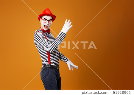 Mime male in white gloves and red hat looking at camera on orange background 61918965