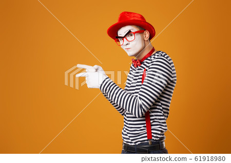 Mime in red hat and in vest pointing with his hand to side on orange background 61918980