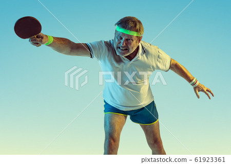 Senior man playing table tennis in sportwear on gradient background and neon light Senior man playing table tennis in sportwear on gradient background and neon light 61923361