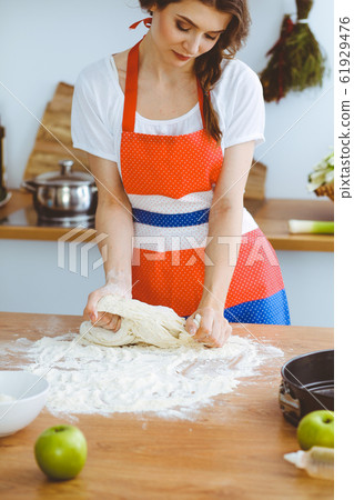 Young brunette woman cooking pizza or handmade pasta in the kitchen. Housewife preparing dough on wooden table. Dieting, food and health concept 61929476