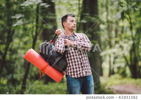 guy with backpack, traveller, hipster standing in woods, Hiking, Forest, Journey. Caucasian tourist man packs rucksack, takes things. Man having break during hike in wood. looking into travel bag 61931382