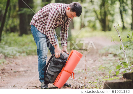 Hiker holding his camping backpack. traveler opening backpack while traveling in beautiful wood. Theme hiking and travel. Man traveling in forest with backpack. Active healthy man hiking in forest 61931383
