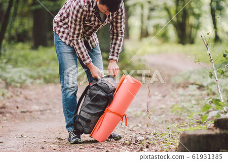 guy with backpack, traveller, hipster standing in woods, Hiking, Forest, Journey. Caucasian tourist man packs rucksack, takes things. Man having break during hike in wood. looking into travel bag 61931385