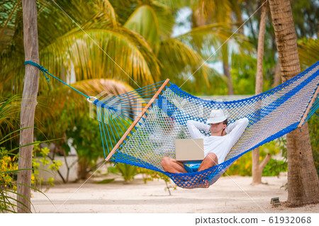 Young man with laptop at hammock on tropical vacation Young man with laptop at hammock on tropical vacation 61932068