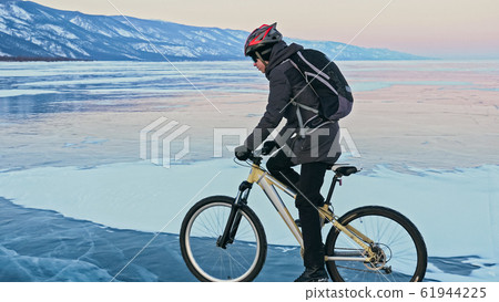 Man is riding bicycle on the ice. Ice of frozen Lake Baikal. Tee Man is riding bicycle on the ice. Ice of frozen Lake Baikal. Tee 61944225