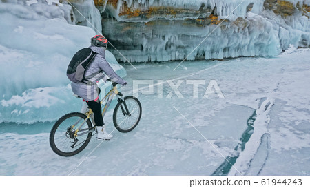 Woman is riding bicycle near the ice grotto. The rock with ice c 61944243