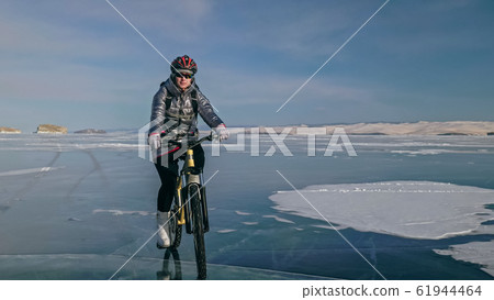 Woman is riding bicycle on the ice. Tires on bike are covered wi 61944464