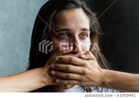 Close Up of Young Woman with Green Eyes Covering Mouth with Hands 61950491