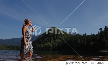 Woman walk on water on pier in sunglasses and a boho silk shawl. Girl rest on flood wood underwater dock. The pavement is covered with water in lake. Woman walk on water on pier in sunglasses and a boho silk shawl. Girl rest on flood wood underwater dock. The pavement is covered with water in lake. 61950688