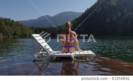 Woman lie on a sunbed in sunglasses and swimming suit. Girl rest on a flood wood underwater pier. The pavement is covered with water in lake. Woman lie on a sunbed in sunglasses and swimming suit. Girl rest on a flood wood underwater pier. The pavement is covered with water in lake. 61950692