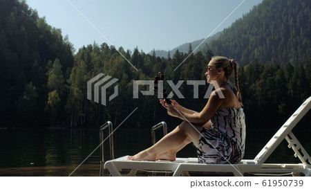 Woman shooting on handheld film gimbal stabilization for smartphone. Girl lie sunbed on pier make selfie. Blogger broadcast video vlogging. 61950739