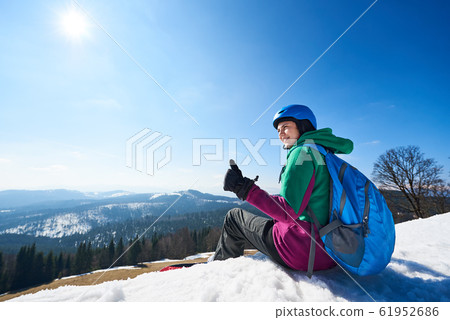 Female snowboarder resting on snowy summit shows thumb-up gesture. Winter sports concept. Female snowboarder resting on snowy summit shows thumb-up gesture. Winter sports concept. 61952686