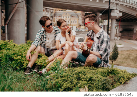 Young People With A Guitar Have Fun Sitting On The Grass Young People With A Guitar Have Fun Sitting On The Grass 61955543