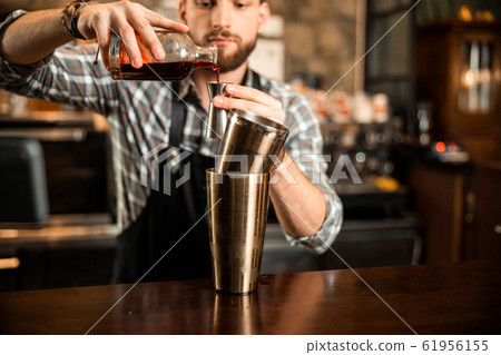 Young barman holding a bottle and measuring cup 61956155
