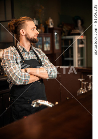 Smiling young bartender is crossing his arms 61956238