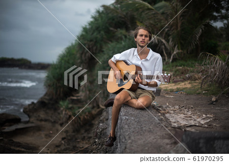 Romantic young man with a guitar on the beach Romantic young man with a guitar on the beach 61970295