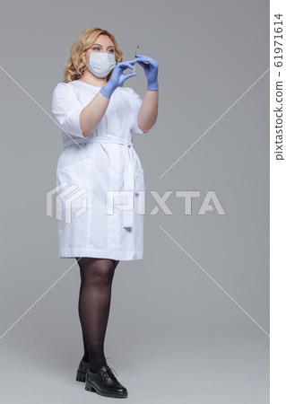 Female doctor in face mask holding syringe. Portrait of young woman doctor or nurse in protective gloves holding an injection Female doctor in face mask holding syringe. Portrait of young woman doctor or nurse in protective gloves holding an injection 61971614