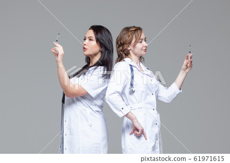 Two female doctors standing back-to-back hold ready-to-inject syringes Two female doctors standing back-to-back hold ready-to-inject syringes 61971615