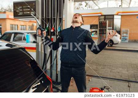 Depressed man cries on gas station, fuel filling Depressed man cries on gas station, fuel filling 61973123