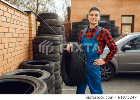 Male worker at the stack of tyres, tire service Male worker at the stack of tyres, tire service 61973247