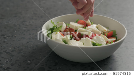 man hands salting salad with mozzarella, cherry tomatoes and frisee leaves in white bowl on terrazzo surface man hands salting salad with mozzarella, cherry tomatoes and frisee leaves in white bowl on terrazzo surface 61974516