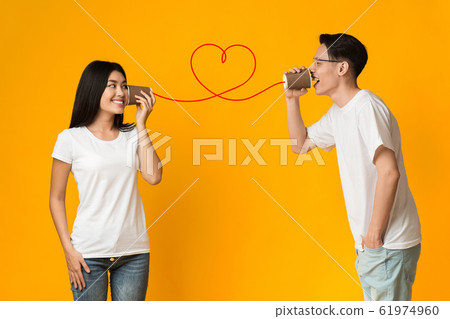 Asian guy telling girlfriend about love, using can phone Asian guy telling girlfriend about love, using can phone 61974960