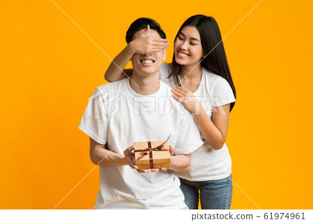 Smiling asian girl covering boyfriend eyes, greeting with valentine Smiling asian girl covering boyfriend eyes, greeting with valentine 61974961