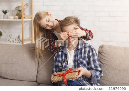 Sister Covering Brother's Eyes Giving Birthday Gift Sitting At Home 61974990