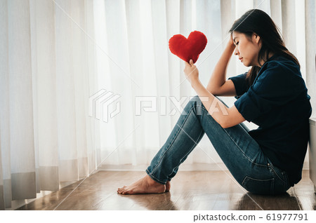 sad Asian woman sitting by the bed holding red heart 61977791