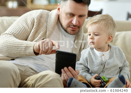 Father with boy using device on couch 61984240