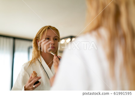 Stunning woman standing in front of the mirror applying makeup 61991595