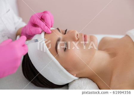 Female cosmetologist making injection in lady forehead Female cosmetologist making injection in lady forehead 61994356