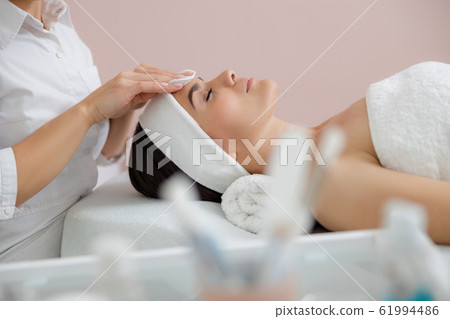 Cosmetologist removing impurities from lady face with cotton pads Cosmetologist removing impurities from lady face with cotton pads 61994486