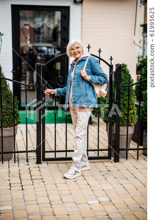 Happy elderly female at gate to house stock photo Happy elderly female at gate to house stock photo 61995625