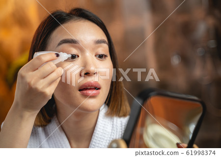 Asian girl is using eye drops indoors Asian girl is using eye drops indoors 61998374