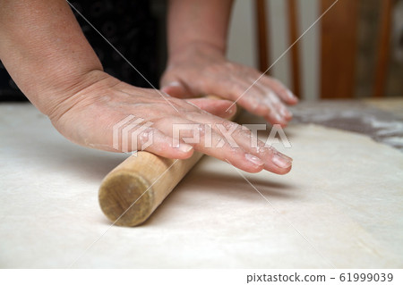 Senior woman hands are rolling out dough in flour Senior woman hands are rolling out dough in flour 61999039