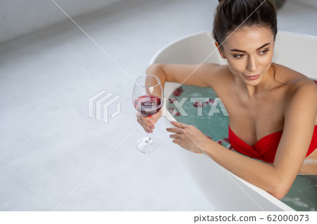 Girl sitting in a bathtub with rose petals Girl sitting in a bathtub with rose petals 62000073