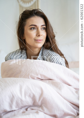 Woman wrapped in a duvet looking away Woman wrapped in a duvet looking away 62001322