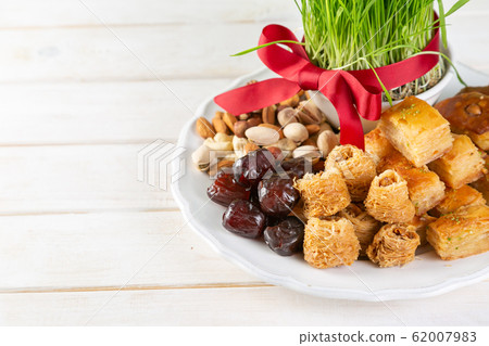 Nowruz holiday concept - grass, baklava sweets, nuts and seeds Nowruz holiday concept - grass, baklava sweets, nuts and seeds 62007983
