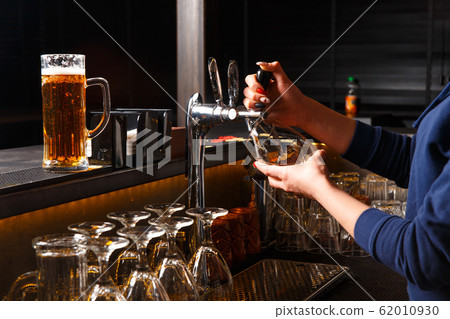 Hands of female bartender pouring from tap fresh beer into the glass Hands of female bartender pouring from tap fresh beer into the glass 62010930