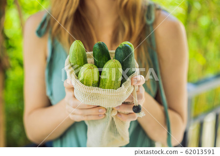 Cucumbers in a reusable bag in the hands of a young woman. Zero waste concept Cucumbers in a reusable bag in the hands of a young woman. Zero waste concept 62013591