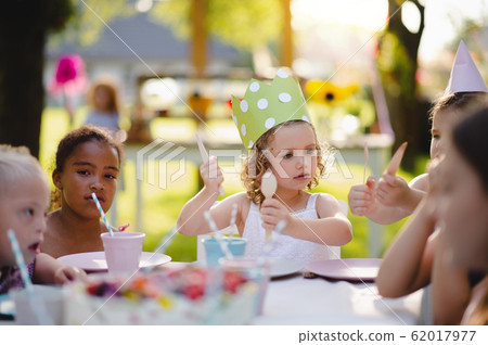 Small children sitting at the table outdoors on garden party, eating. 62017977