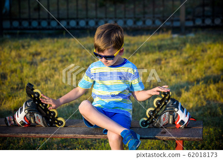 Little handsome boy in roller-blades sits in bench 62018173