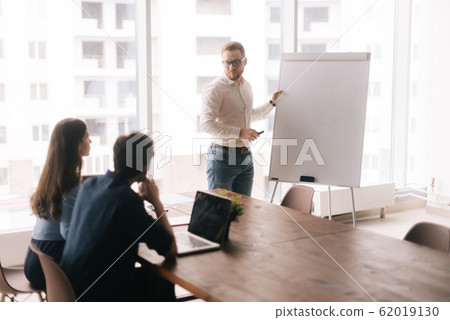 Young confident businessman presenting new project to partners on whiteboard 62019130