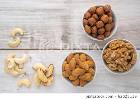 Different nuts in white bowls on wood table 62023119