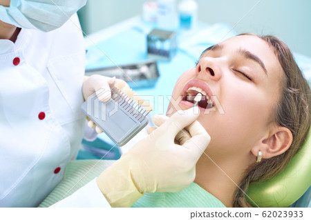 Beautiful smile and white teeth of a young woman. Matching the shades of the implants or the process of teeth whitening. Teeth palette. 62023933