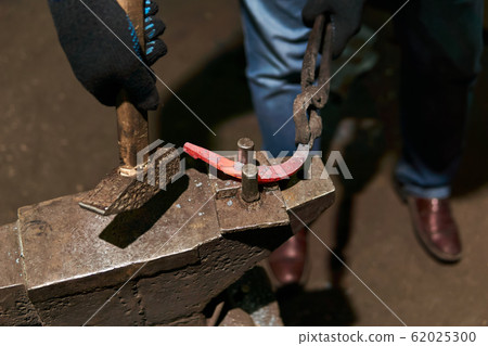 blacksmith forges a horseshoe, close-up 62025300