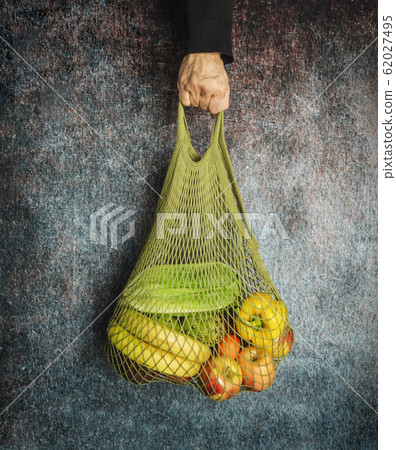 A man's hand holds a green string bag with fresh 62027495